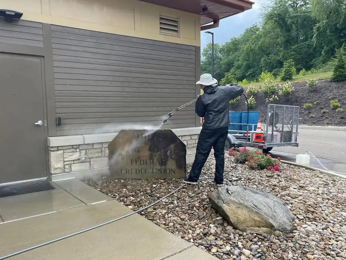 Untitled design (1) Power Clean technician power washing the concrete sign at a bank in Central Ohio