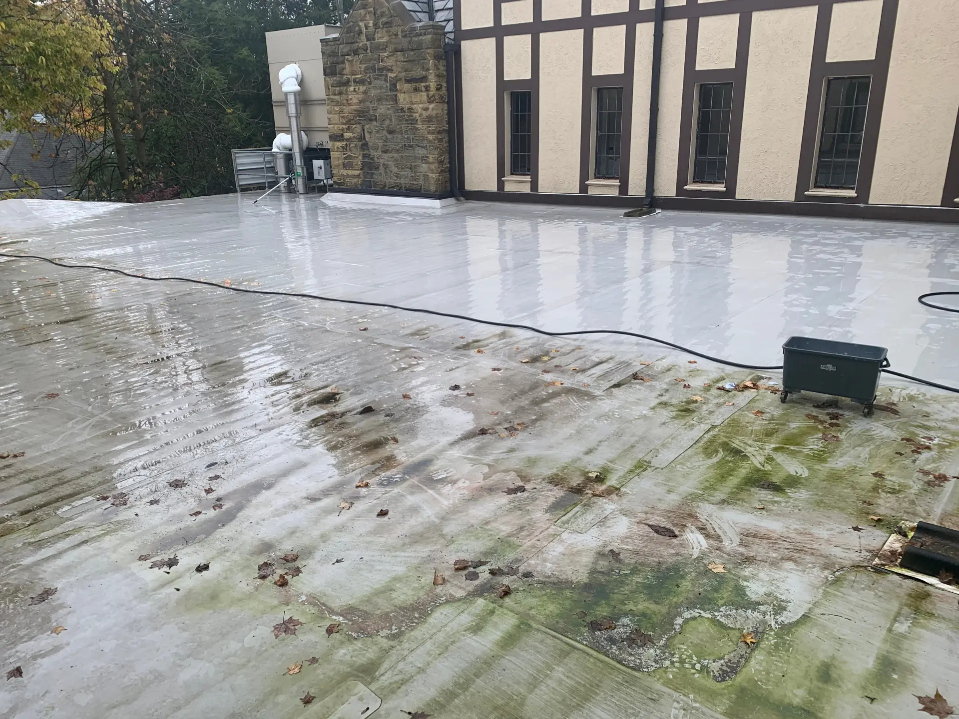 power clean in process of cleaning the roof of commercial building with part of the roof covered in green algae and grime