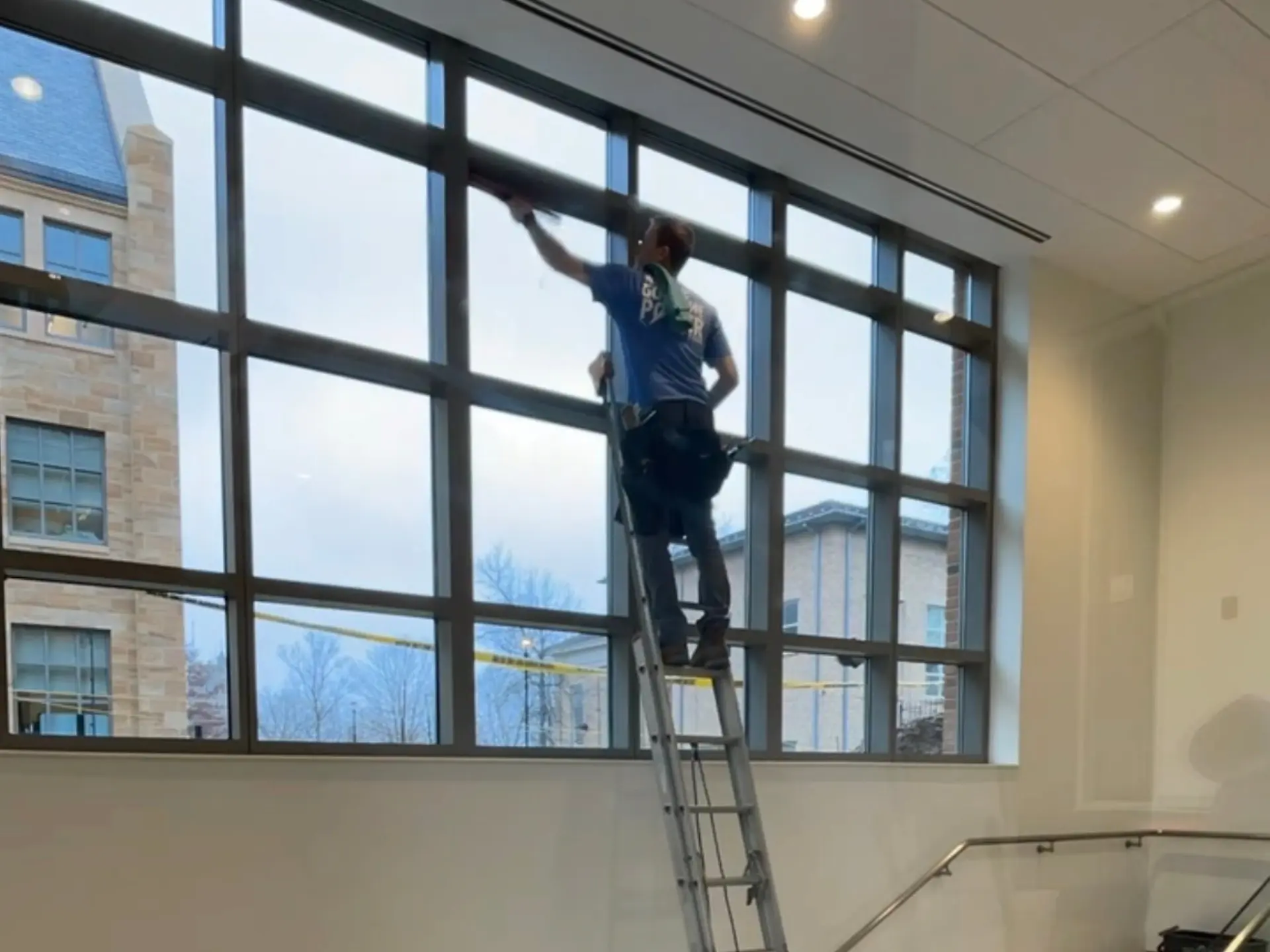 Power Clean technician on a ladder balanced on a staircase to clean the high windows of a commercial building