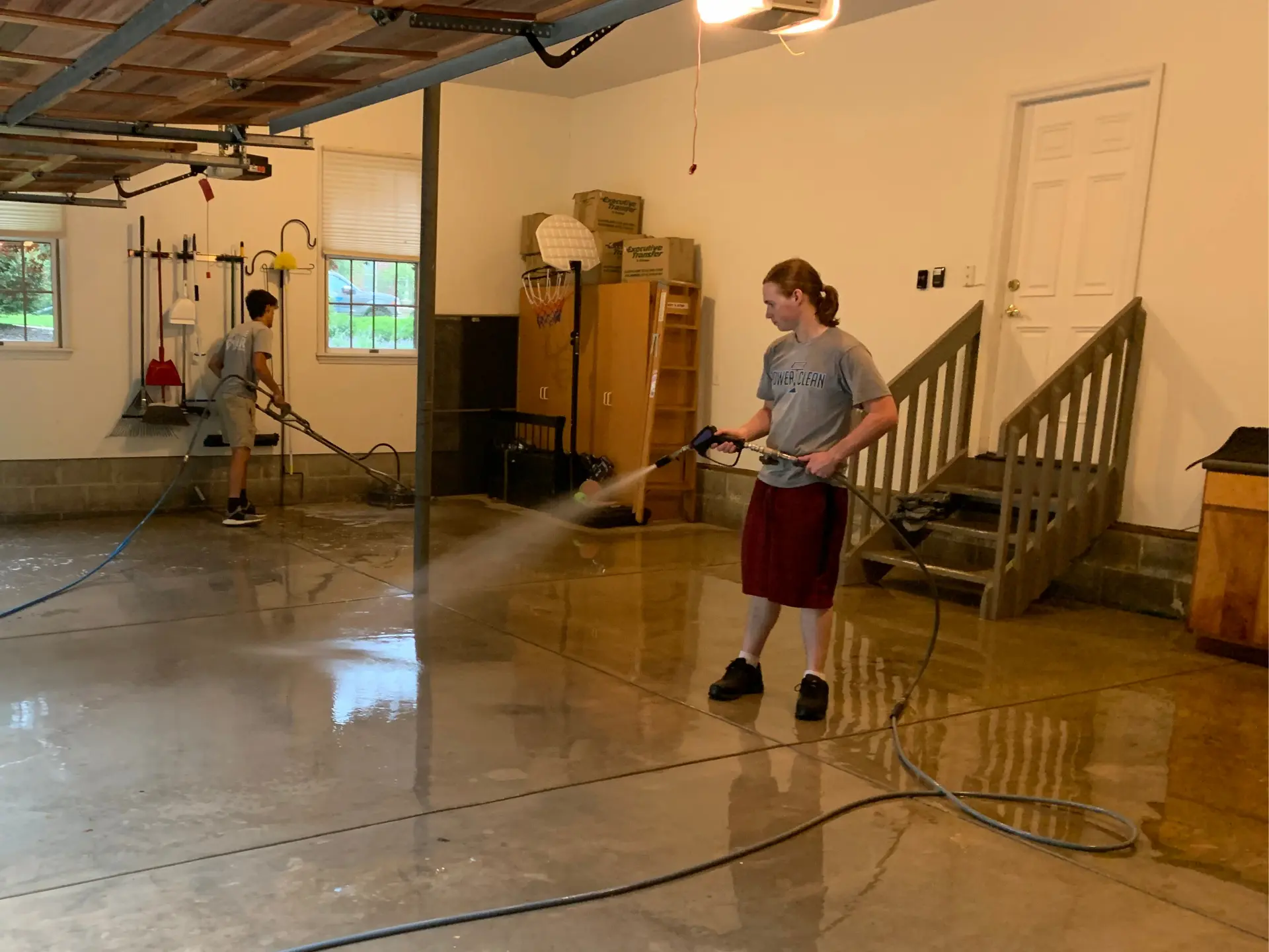 Two power clean technicians pressure washing inside a garage area