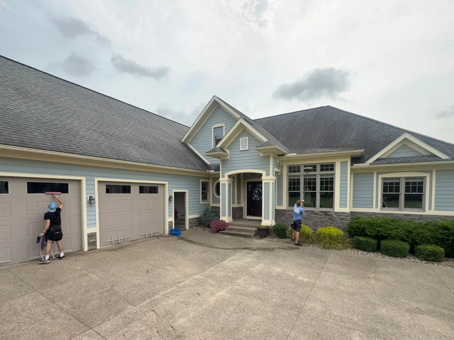 residential-window-cleaning-front-entry.webp Two power clean technicians cleaning the exterior front windows of a house